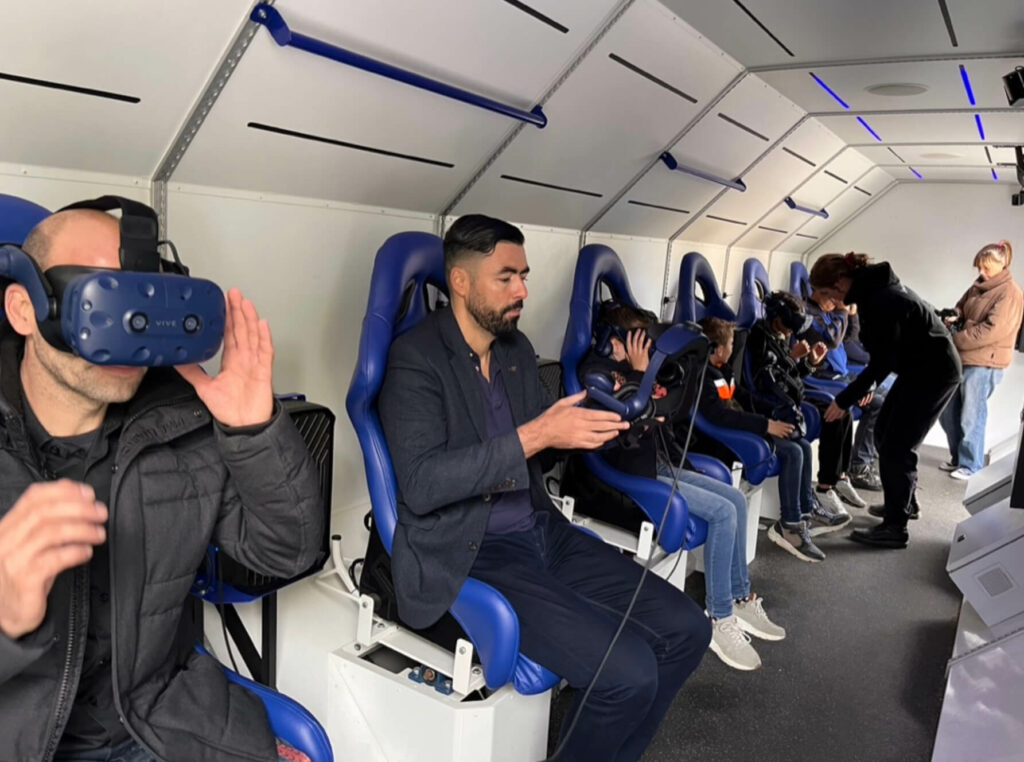 Mensen met een Virtual reality bril in de Spacebuzz. Witte achtergrond, blauwe stoelen
